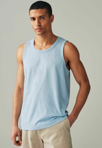 Lysblå bomulds tanktop med en rund halsudskæring og en lille logo detalje på venstre bryst, parret med beige shorts. Blød tekstur, afslappet pasform.