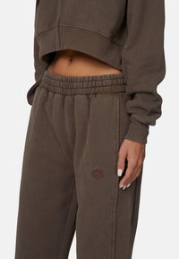 Brązowy, krótkie sweter z prążkowanymi mankietami i ściągaczem, w zestawie z dopasowanymi brązowymi spodniami dresowymi na elastycznym pasie, które posiadają subtelny detal z logo.