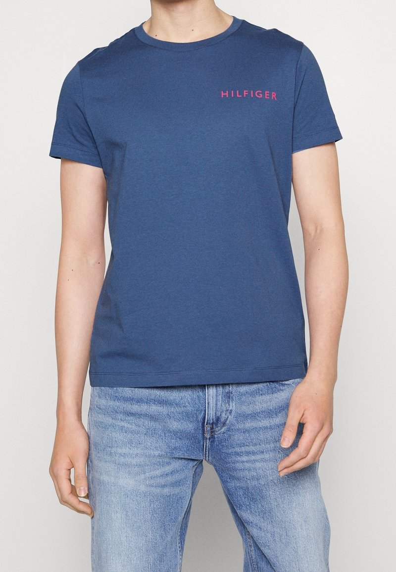 Navy blue cotton t-shirt with short sleeves, round neckline, and a pink "HILFIGER" logo on the left chest. Casual fit.