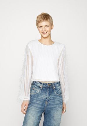 White cropped top with textured body and sheer, long sleeves. Paired with high-waisted blue denim jeans.