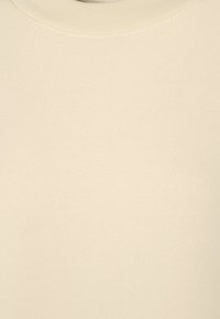 Dettaglio di un tessuto a coste di colore crema con scollatura rotonda, che mostra una fine trama a maglia.