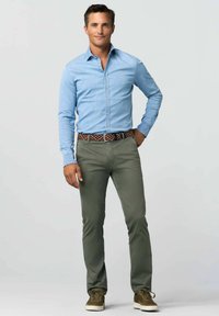 Himmelblaues Hemd mit langen Ärmeln, grüne Hose und einen gemusterten Gürtel. Die Schuhe sind dunkelgrüne Sneakers mit weißen Sohlen.