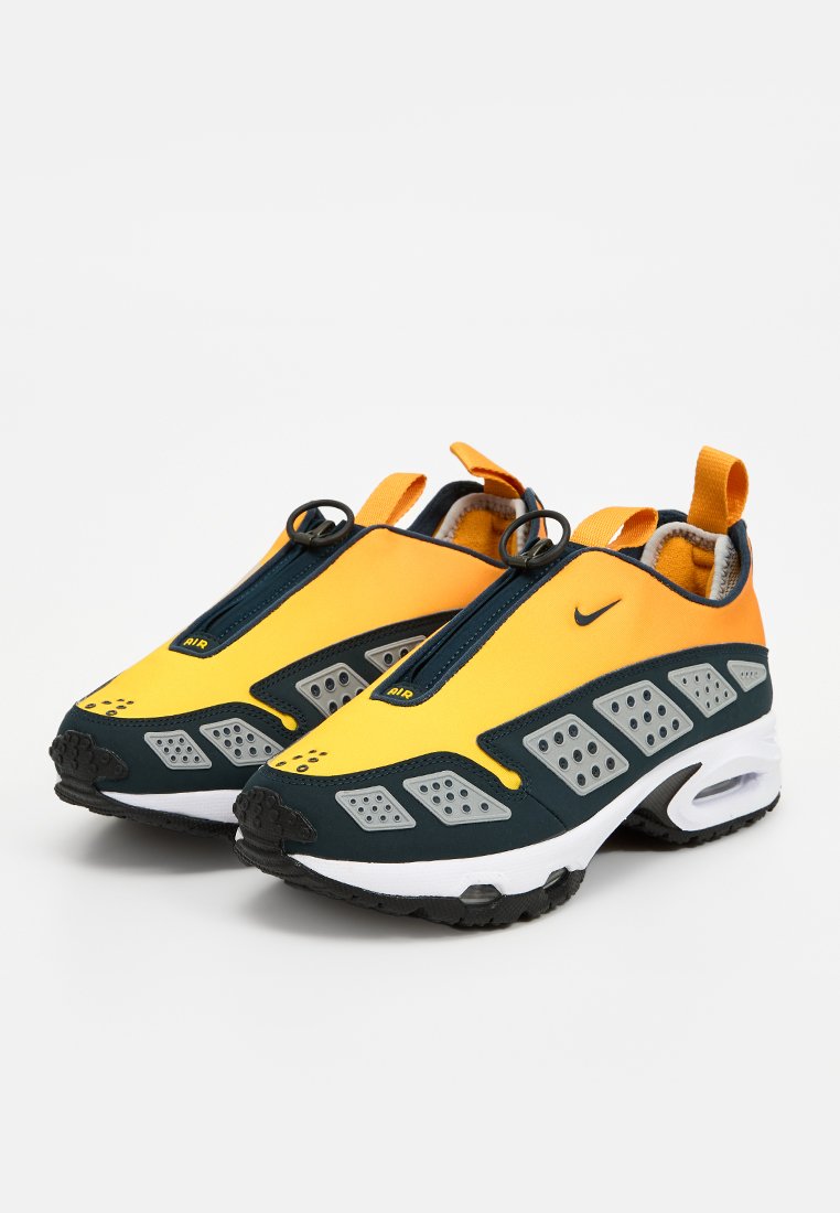 Zapatillas deportivas con parte superior amarilla, detalles en azul marino y paneles perforados grises. Suela de goma negra con característica de amortiguación de aire y tiradores.