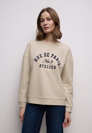 Sudadera beige con cuello redondo, con texto en azul oscuro: "RUE DE PARIS No.9 ATELIER." Tejido suave, ajuste relajado y puños acanalados.