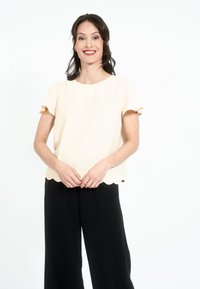 Kreemiline sakiline äärega pluus lühikeste varrukatega, kombineeritud vabade mustade pükstega. Sile tekstuur, minimalistlik disain.