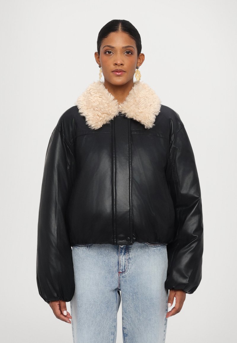Veste en cuir noire courte avec un col en fourrure beige duveteux, dotée de longues manches bouffantes et d'une taille légèrement cintrée.