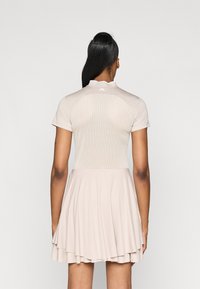 Beiges Sportkleid mit tailliertem Oberteil und perforiertem Rücken, kurzen Ärmeln und einem ausgestellten, schichtenrock. Leichter, glatter Stoff.