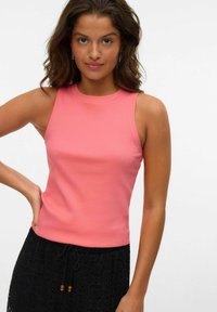 Top aderente a costine di colore rosa corallo, con scollatura tonda e senza maniche, abbinato a una gonna nera in pizzo.