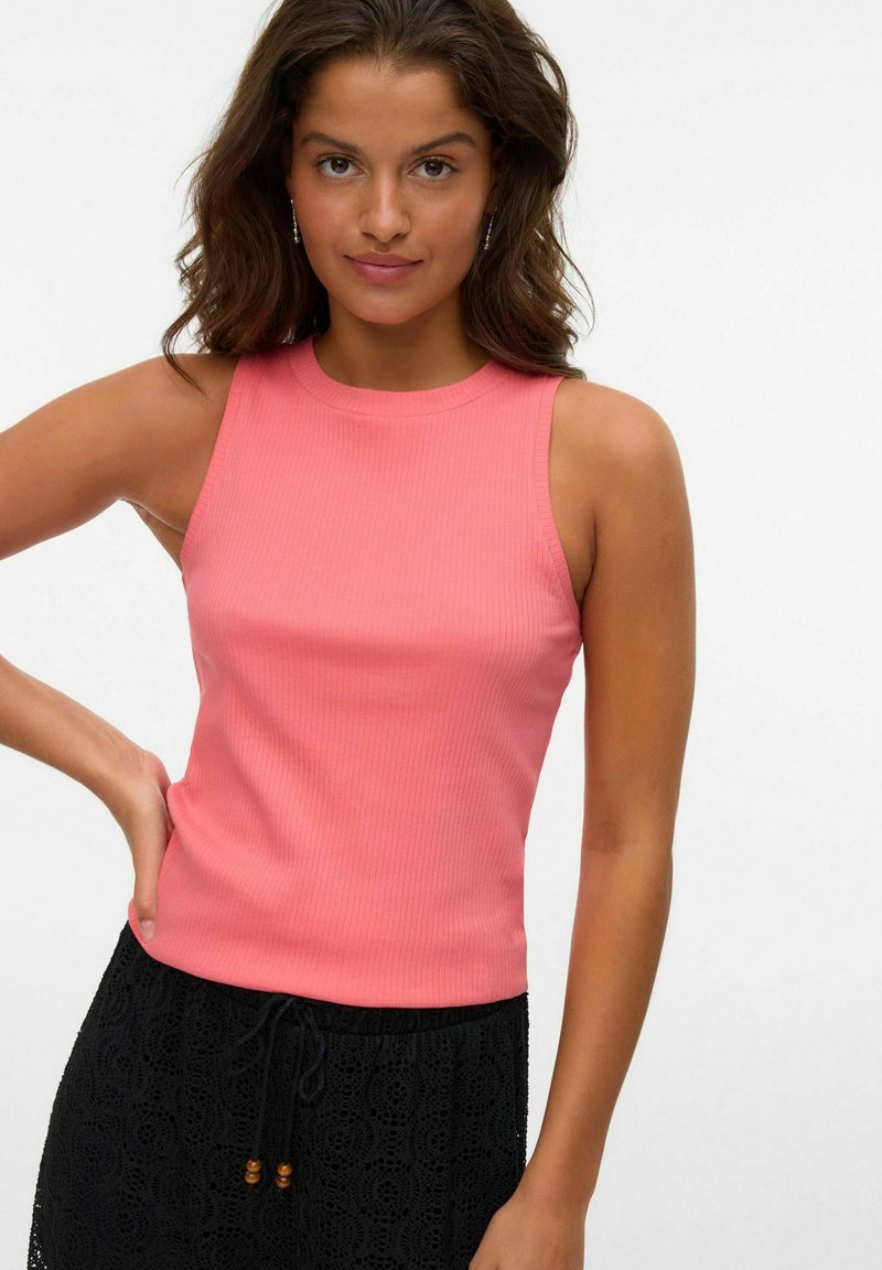 Top aderente a costine di colore rosa corallo, con scollatura tonda e senza maniche, abbinato a una gonna nera in pizzo.