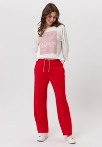 Pantalon large rouge avec taille à cordon, associé à un haut à manches longues blanc avec un design graphique « FASHION » en rouge.