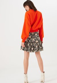 Oranje cropped sweatshirt met ballonmouwen, gecombineerd met een zwarte rok met ruffles en bloemenpatronen, en witte enkellaarsjes met studs.