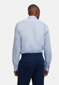 Himmelblaues Langarmhemd mit strukturierter Oberfläche, Knopfmanschetten und Kragen, kombiniert mit dunkelblauen maßgeschneiderten Hosen mit Taschen.