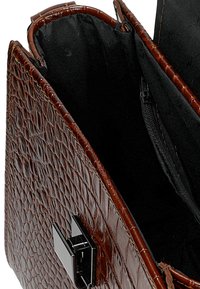 Bruine handtas van krokodillenleer met een gestructureerd ontwerp, voorzien van een zwarte stoffen voering en een zilveren metalen sluiting.