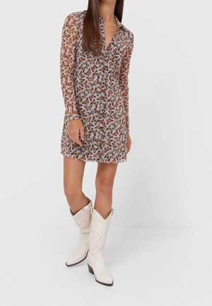 Durchsichtiges, langärmeliges Kleid mit Schmetterlingsdruck in erdigen Tönen. Verfügt über einen Kragen und eine Knopfleiste. Kombiniert mit weißen, westernmäßigen Stiefeln.