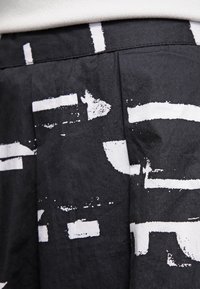 Tessuto nero con motivi astratti bianchi; presenta plissettature e una vita. La texture appare liscia e leggermente lucida.