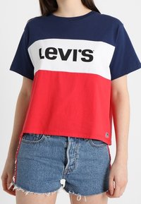 Tričko s krátkým rukávem v barvách červené, bílé a modré, s logem "Levi's". Nosené s roztrhanými modrými džínovými šortkami. Jednoduchý, ležérní design.