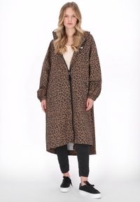Barna leopárdmintás kabát kapucnival, hosszú ujjú, laza szabású, fekete nadrággal és fekete sportcipővel párosítva.