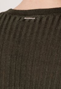 Maglione a coste verde scuro con una finitura testurizzata e un dettaglio con logo in argento sul collo. Progettato per un look casual.