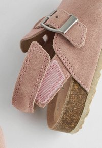 Sandale en daim rose avec une boucle métallique, une sangle ajustable et une semelle intérieure texturée. Semelle en liège avec des accents marron clair.