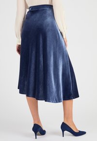Falda midi de terciopelo azul marino con forma acampanada, textura suave y cinturilla oculta, combinada con unos zapatos de tacón a juego.