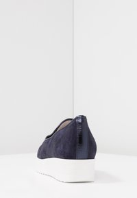 Navy semišová bota s kontrastní lesklou patou, vybavená bílou kuželovou podrážkou a texturovanou boční stranou, pohled zezadu.