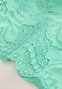 Közeli kép menta zöld csipkeanyagról, virágmintákkal és hullámos széllel.