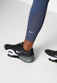 Czarno-białe buty sportowe Nike o plecionej strukturze, z grubą szarym obcasem i skośnym wzornictwem. Noszone z granatowymi legginsami.