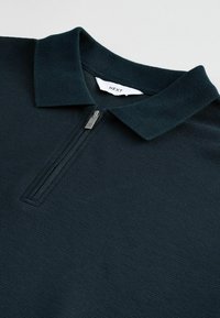 Marine polo skjorte med lynlås krave. Fremstillet af struktureret stof, med et syet mærke indeni. Rent design, let vægt.