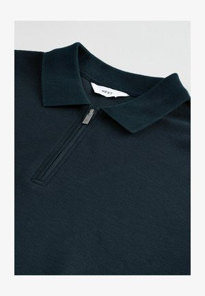 Marineblauwe polo met een ritskraag. Gemaakt van gestructureerde stof, met een gestikt label aan de binnenkant. Schoon ontwerp, lichtgewicht uitstraling.