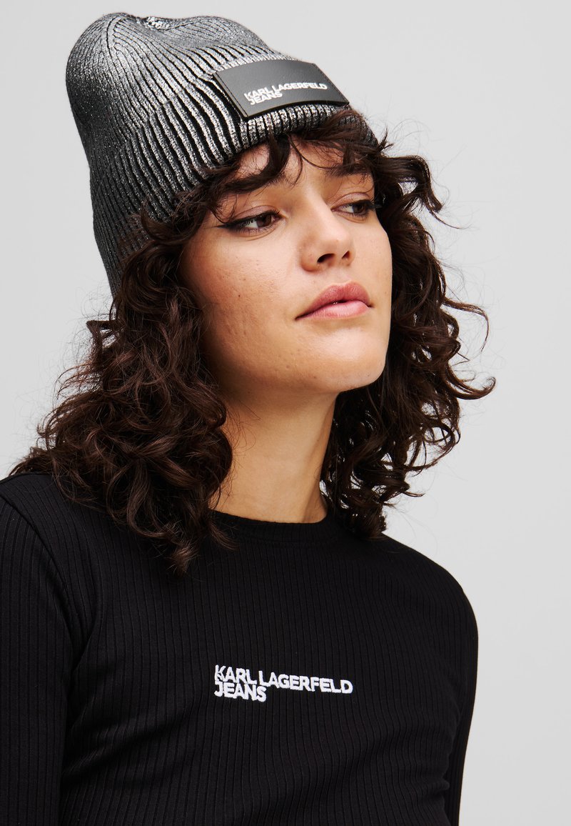Crna rebrasta majica s bijelim vezom "KARL LAGERFELD JEANS". Metalno srebrna pletena kapa s ravnim crnim logotipom.