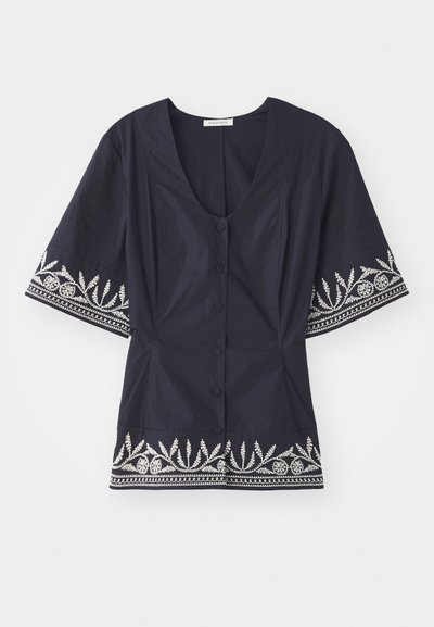 Temno modra bluzica z V-izrezom, kratkimi rokavi in belim cvetličnim vezenjem ob robu in rokavih. Ima gumbasto zapiranje.