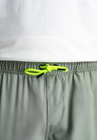 Pantaloni corti verde chiaro con vita elastica, caratterizzati da un vivace cordoncino giallo neon e discreti dettagli di cucitura.