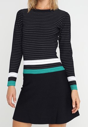 Zwarte jurk met lange mouwen, gemaakt van een gestructureerde stof met horizontale strepen in wit en groen. De rok heeft een uitlopende vorm.