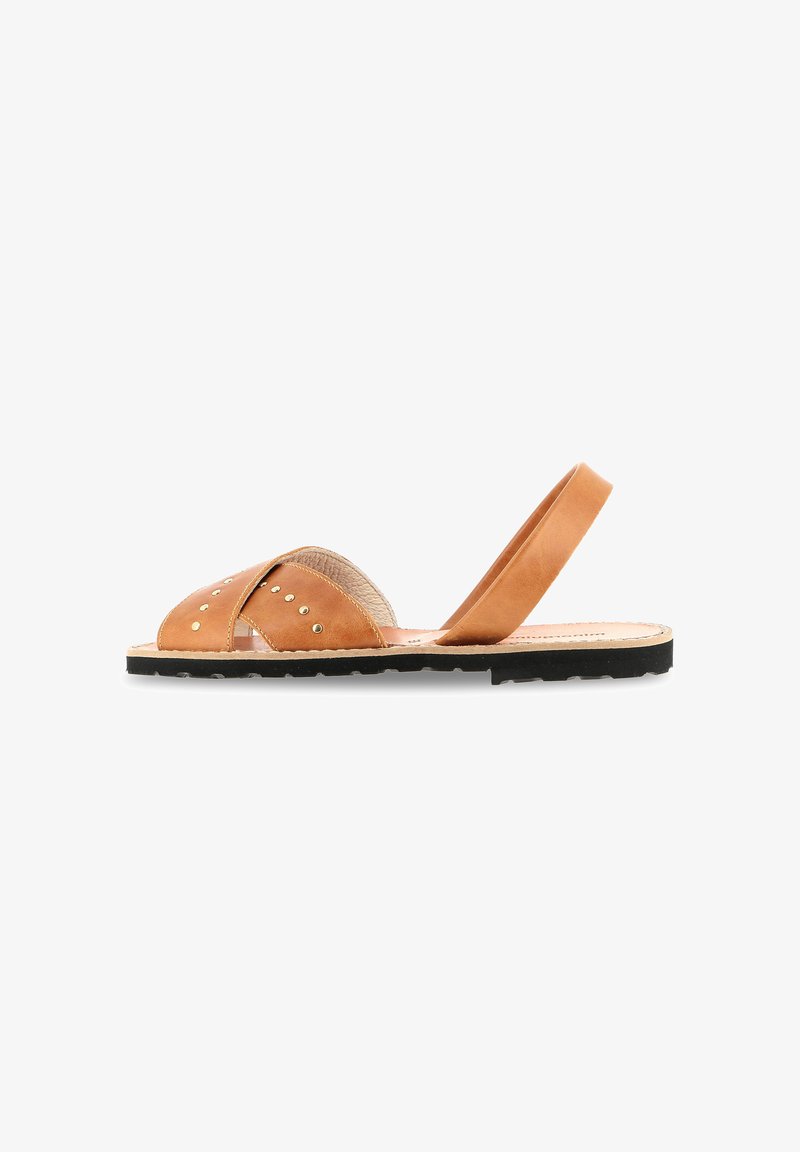 Sandale slingback en cuir tan avec un design à brides croisées, bout rond, accents en clous dorés et semelle en caoutchouc noire. Style plat et décontracté.