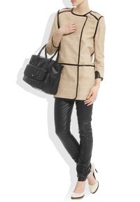 Beige linnekappa med svarta detaljer, slim-fit svarta läderbyxor och vita klackskor. Modellen håller en svart läderhandväska med framficka.