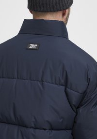 Navy blue puffer jacket with a high collar, quilted texture, and a black label on the back reading "ISOLID."