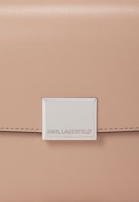 Borsa in pelle liscia di un leggero colore rosa, caratterizzata da una minuteria rettangolare di colore argento con incisione "KARL LAGERFELD", design minimalista e linee pulite.