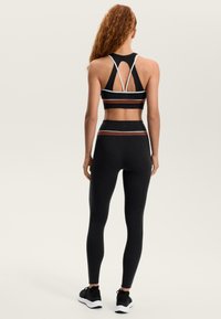 Čierna športová podprsenka a súprava legín s pruhovaným chrbtom, kontrastnými pruhmi v bielej a hrdzavej farbe, s priliehavým dizajnom pre pohodlie.