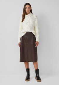 Pull en tricot blanc avec un col haut et un motif en torsades, associé à une jupe midi en cuir marron et des bottines noires à semelles chunky.