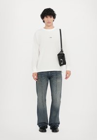 Vit långärmad skjorta med en liten grafik, grå utsvängda jeans och en svart axelväska med metalliska detaljer och ett klaffstängning.
