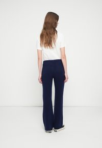Navy ribbed knit flared pants with an elastic waistband, paired with a plain white t-shirt. Model's back is facing the camera.