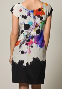 Kortärmad klänning med vit botten och färgglada bläckfläckar i röd, blå och grön, samt en svart avslutning i botten.