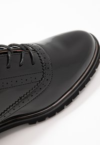 Scarpe eleganti in vernice nera con punta affusolata, dettagli a wingtip e lacci neri. Presentano una suola in gomma testurizzata con battistrada pronunciato.