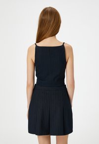 Tuta blu a righe sottili con spalline sottili, corpetto aderente e pantaloni corti con pieghe. Tessuto morbido con una leggera lucentezza.