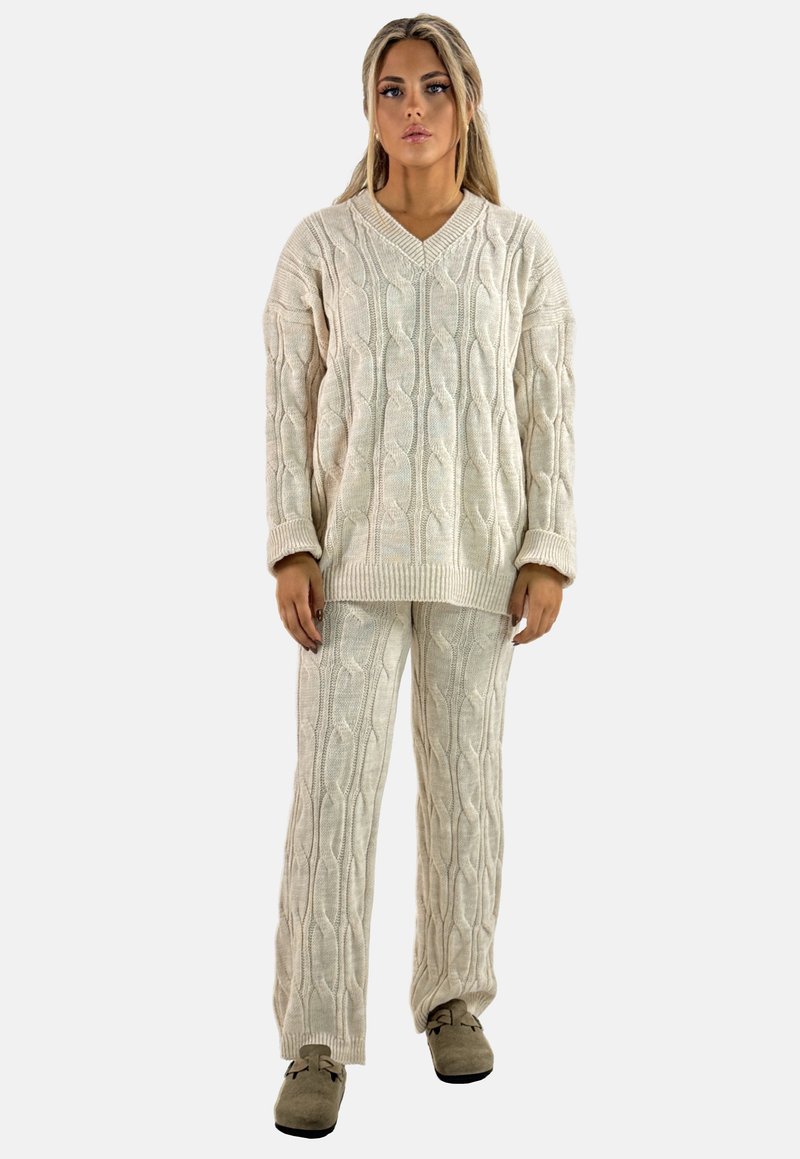 Cremfarbener Kabelstrickpullover und passende Hose im Set, mit V-Ausschnitt, oversized Schnitt und gerippten Bündchen. Sanfte Textur und lockere Form.