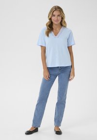 Top corto de manga corta azul claro con un escote de encaje en forma de ondas, combinado con jeans rectos de azul medio y bailarinas negras.