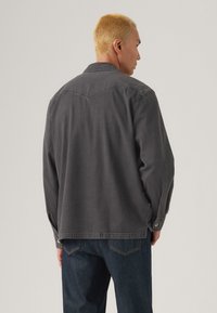 Veste en denim grise avec un col pointu, des poignets à bouton et un design de palette arrière. Présente une coupe décontractée et un tissu subtilement texturé.