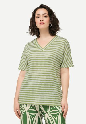 Zeleno-bílý pruhovaný T-shirt s výstřihem do V a krátkým rukávem, vyrobený z texturované tkaniny. Pod ním jsou viditelné vzorované zelené kalhoty.