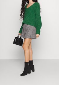 Zielony sweter z dzianiny z dekoltem w serek, mini spódnica w czarno-białą kratkę houndstooth, czarna torebka teksturowana oraz czarne botki na słupku.