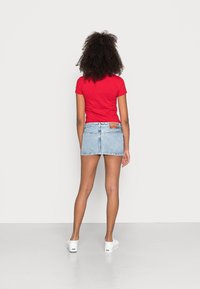 Röd kortärmad t-shirt kombinerad med en ljusblå jeans-minikjol och vita sneakers. Enkel design, inga mönster, med en ren finish.